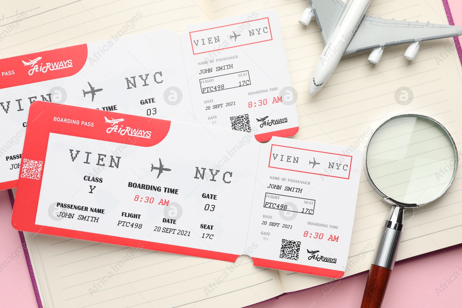 Photo of Travel agency. Flight tickets, plane model, magnifying glass and open notebook on pink background, top view