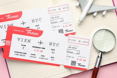 Photo of Travel agency. Flight tickets, plane model, magnifying glass and open notebook on pink background, top view