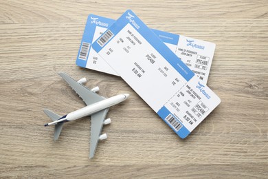 Photo of Travel agency. Flight tickets and plane model on wooden table, flat lay