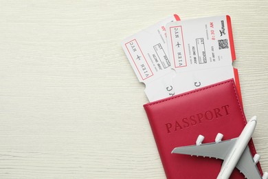 Photo of Travel agency. Flight tickets, passport and plane model on light wooden table, top view. Space for text