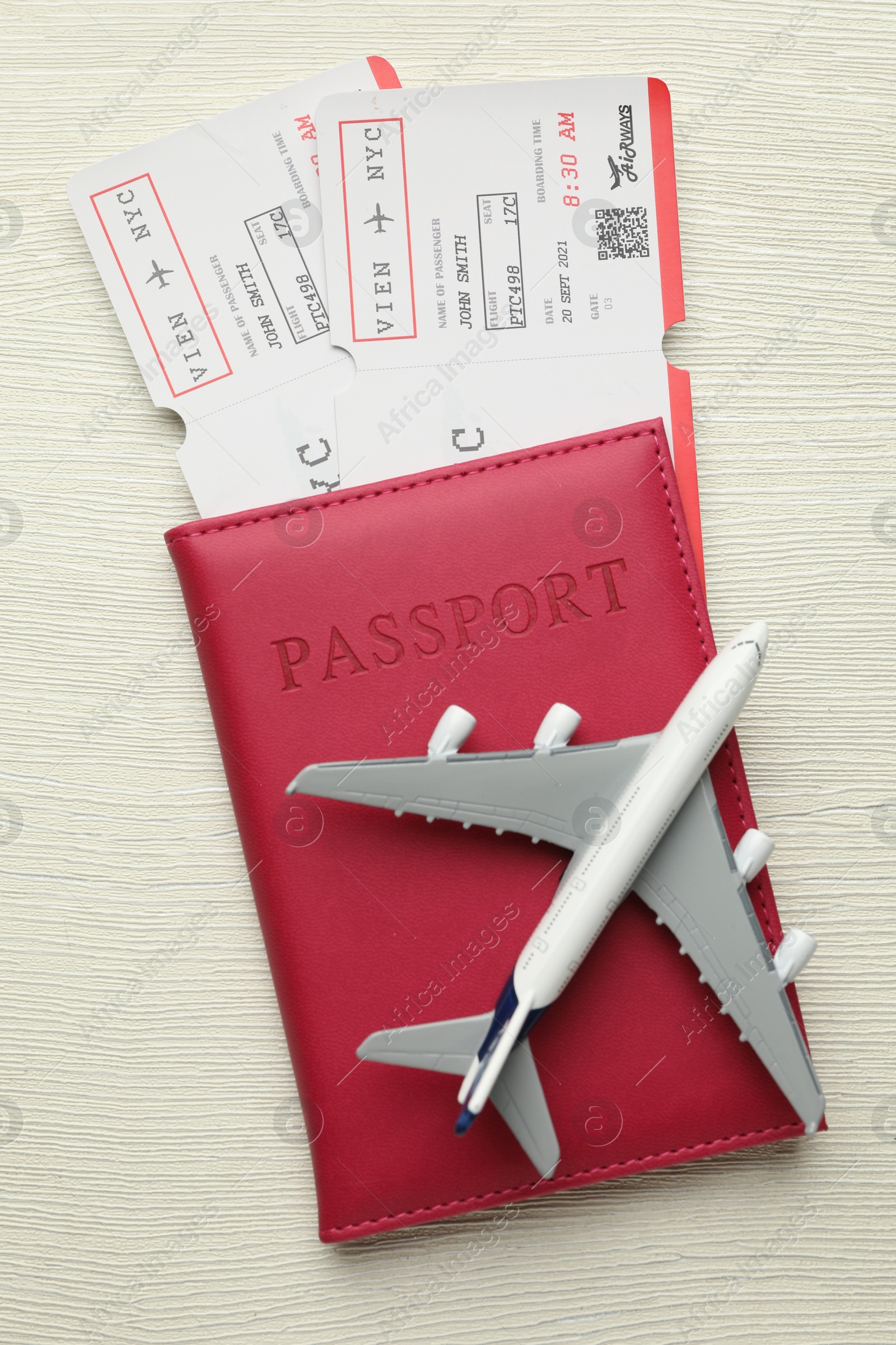 Photo of Travel agency. Flight tickets, passport and plane model on light wooden table, top view