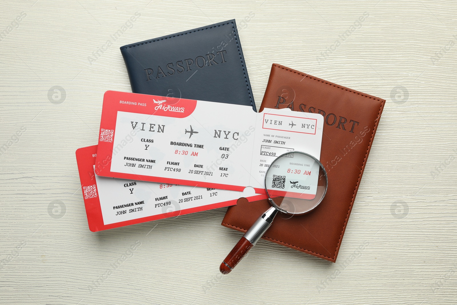 Photo of Travel agency. Flight tickets, passports and magnifying glass on light wooden table, flat lay