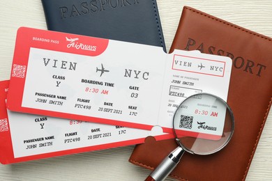 Photo of Travel agency. Flight tickets, passports and magnifying glass on light wooden table, flat lay