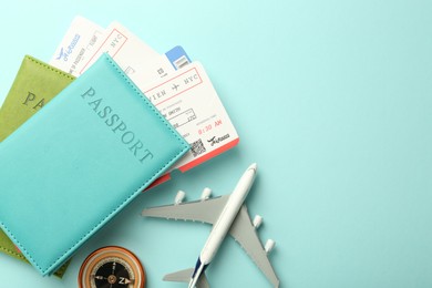 Photo of Passport with tickets, compass and plane model on light blue background, top view. Space for text