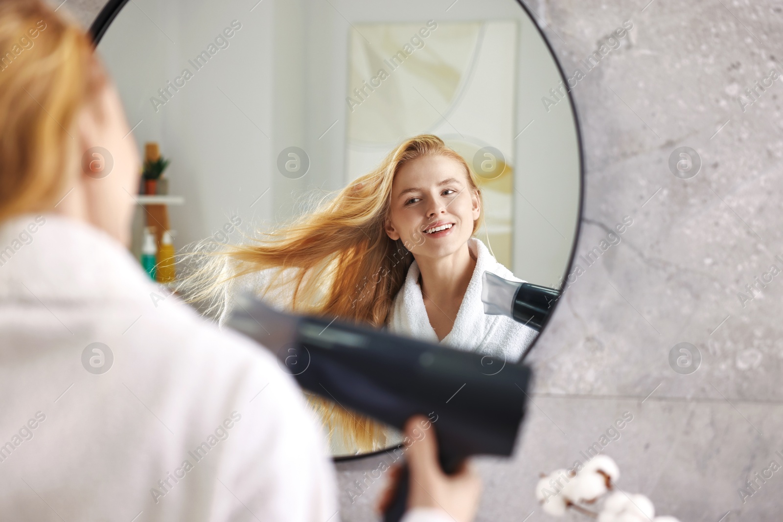 Photo of Beautiful young woman drying her hair near mirror in bathroom