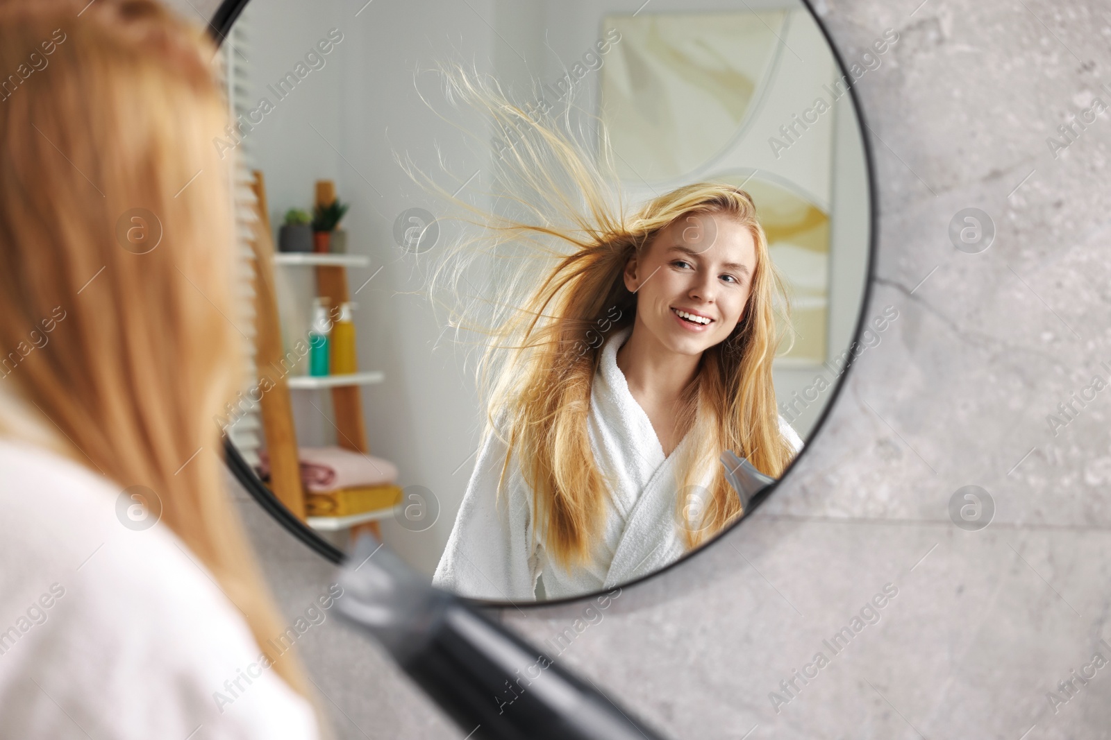 Photo of Beautiful young woman drying her hair near mirror in bathroom