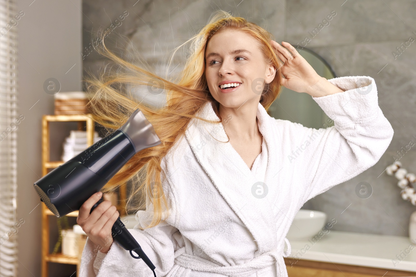 Photo of Beautiful young woman drying her hair in bathroom