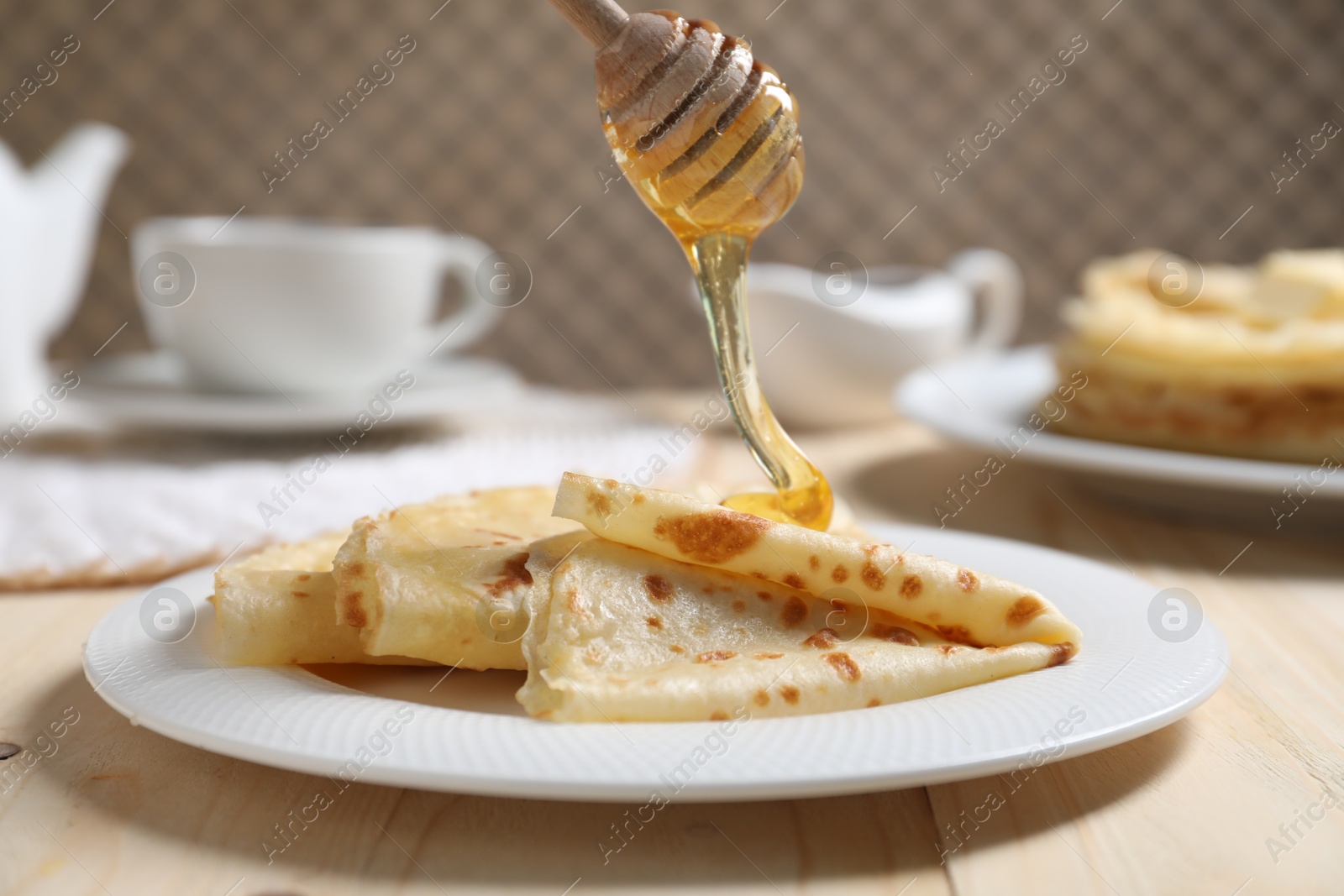 Photo of Pouring honey onto tasty crepes at wooden table, closeup