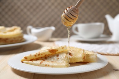 Photo of Pouring honey onto tasty crepes at wooden table, closeup