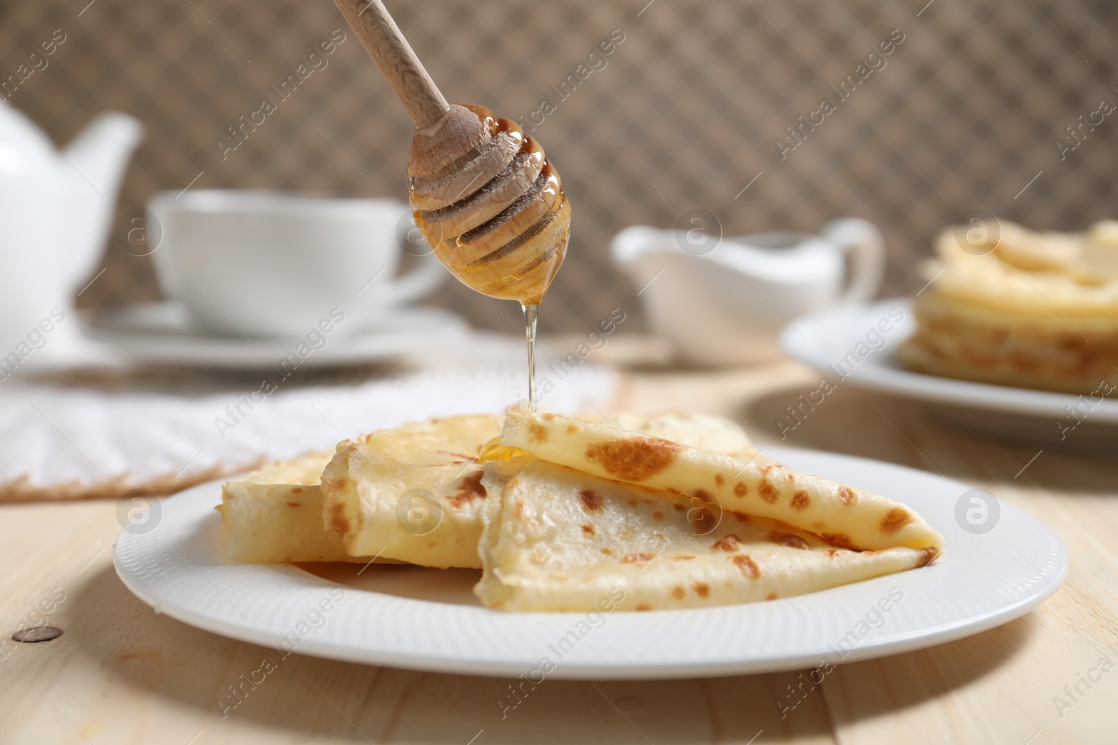 Photo of Pouring honey onto tasty crepes at wooden table, closeup