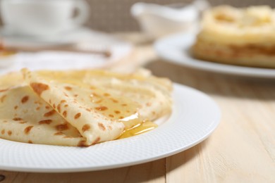 Photo of Tasty crepes with honey on wooden table, closeup