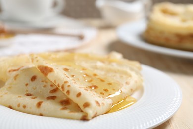 Photo of Tasty crepes with honey on wooden table, closeup