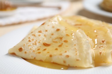 Photo of Tasty crepes with honey on plate, closeup