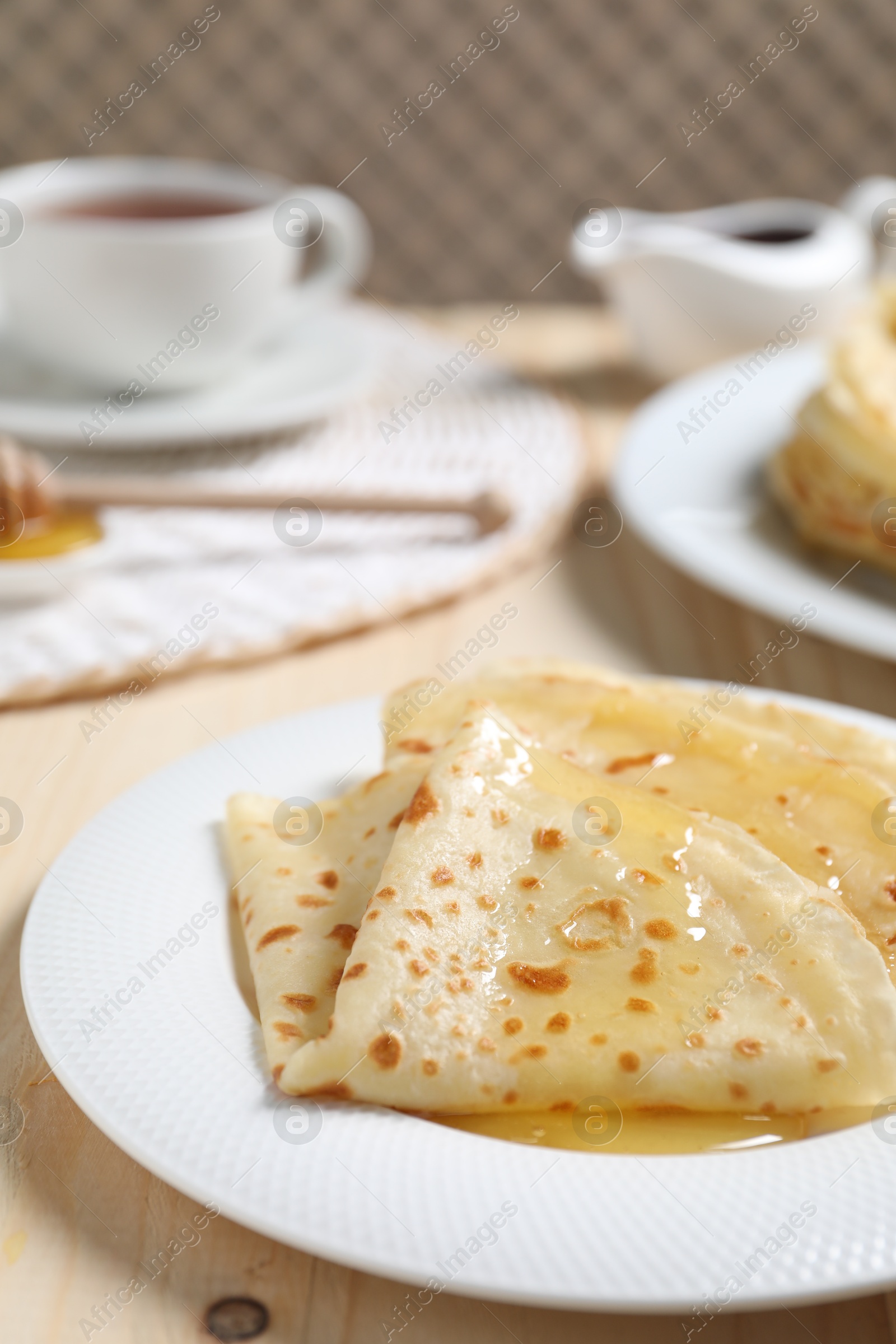 Photo of Tasty crepes with honey on wooden table, closeup