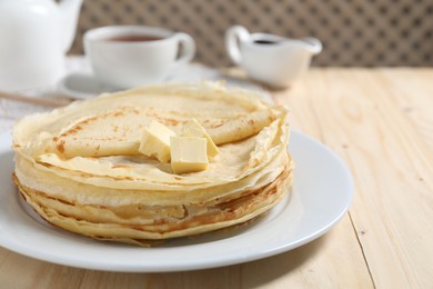 Photo of Stack of tasty crepes with butter on wooden table, closeup