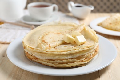 Photo of Stack of tasty crepes with butter on wooden table, closeup