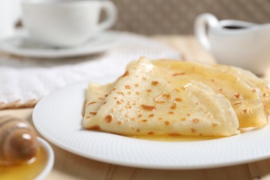 Photo of Tasty crepes with honey on wooden table, closeup