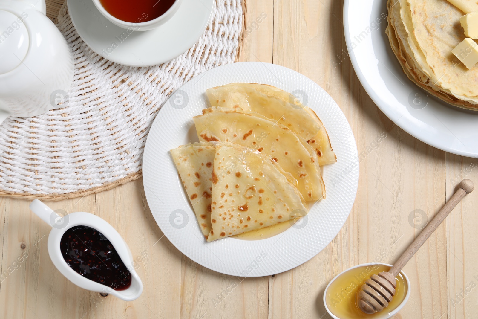 Photo of Tasty crepes with honey served on wooden table, flat lay