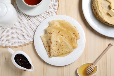 Photo of Tasty crepes with honey served on wooden table, flat lay