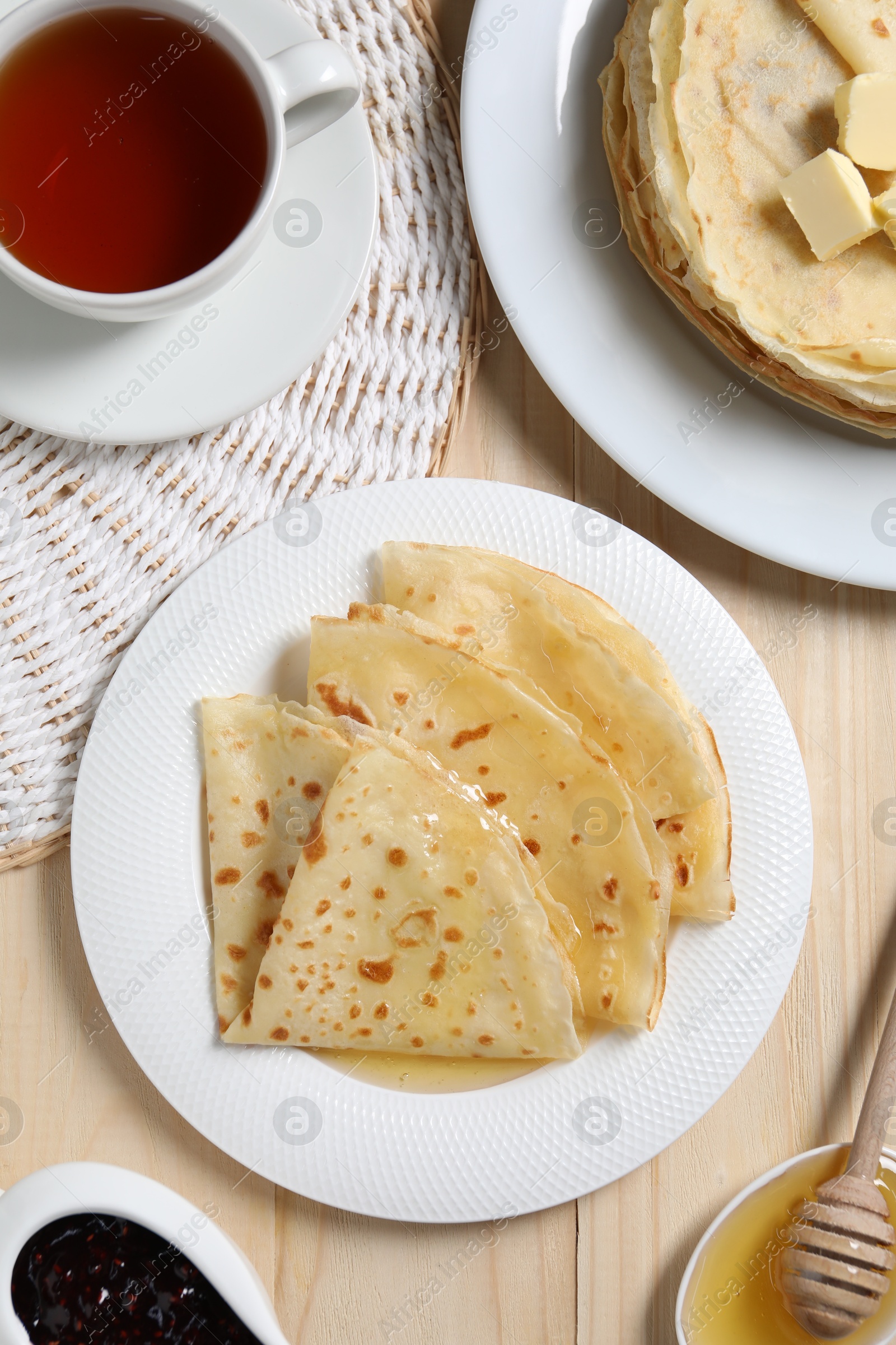 Photo of Tasty crepes with honey served on wooden table, flat lay