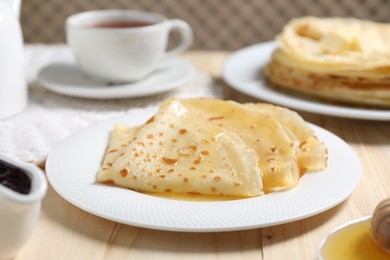 Photo of Tasty crepes with honey on wooden table, closeup