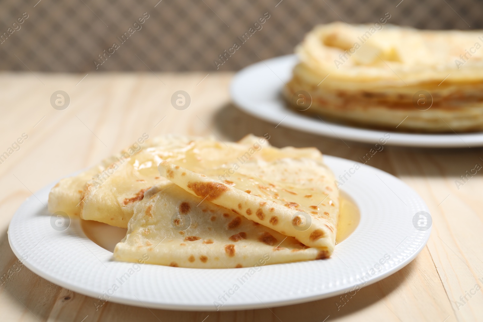 Photo of Tasty crepes with honey on wooden table, closeup