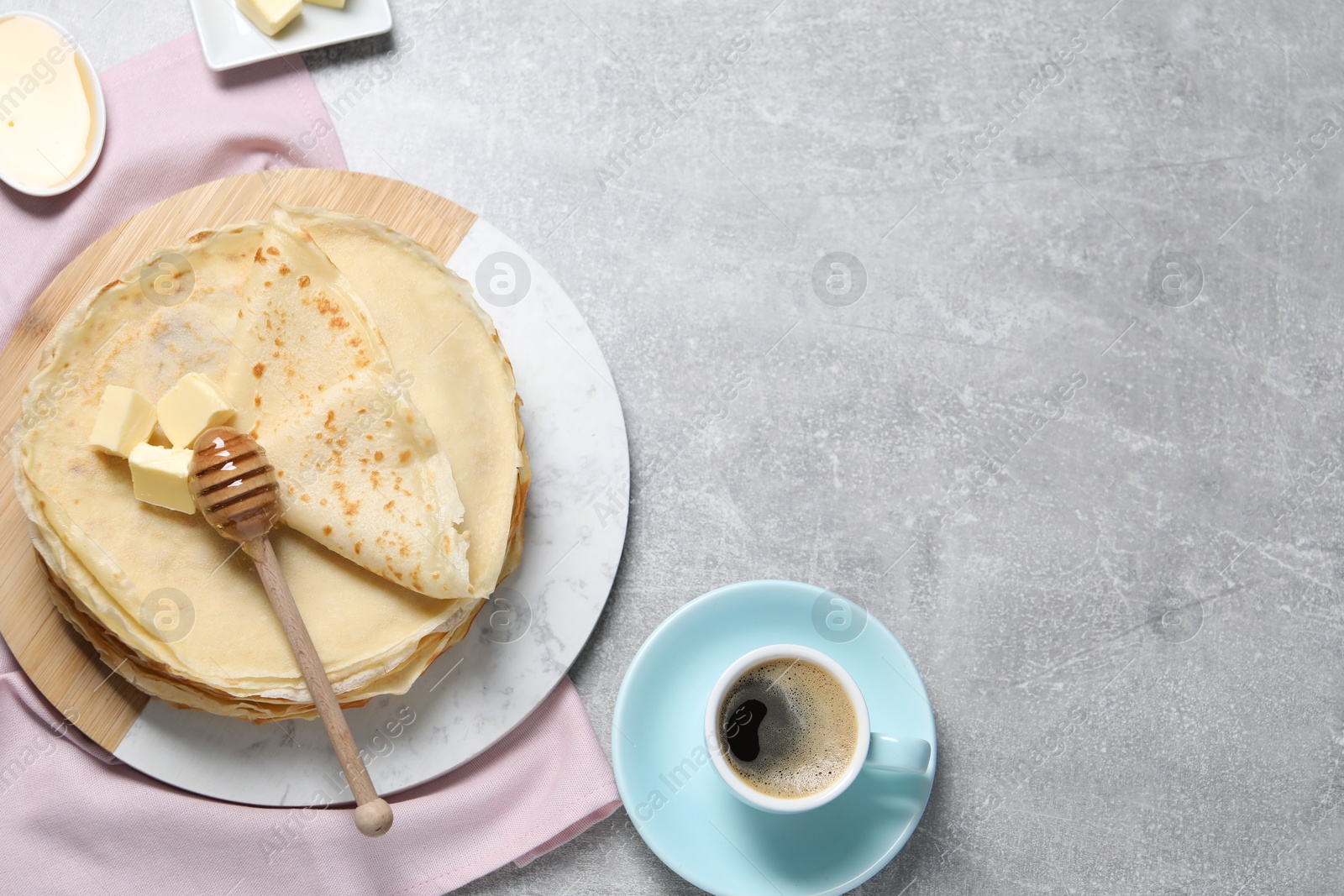 Photo of Tasty crepes with butter and honey served on grey textured table, flat lay. Space for text