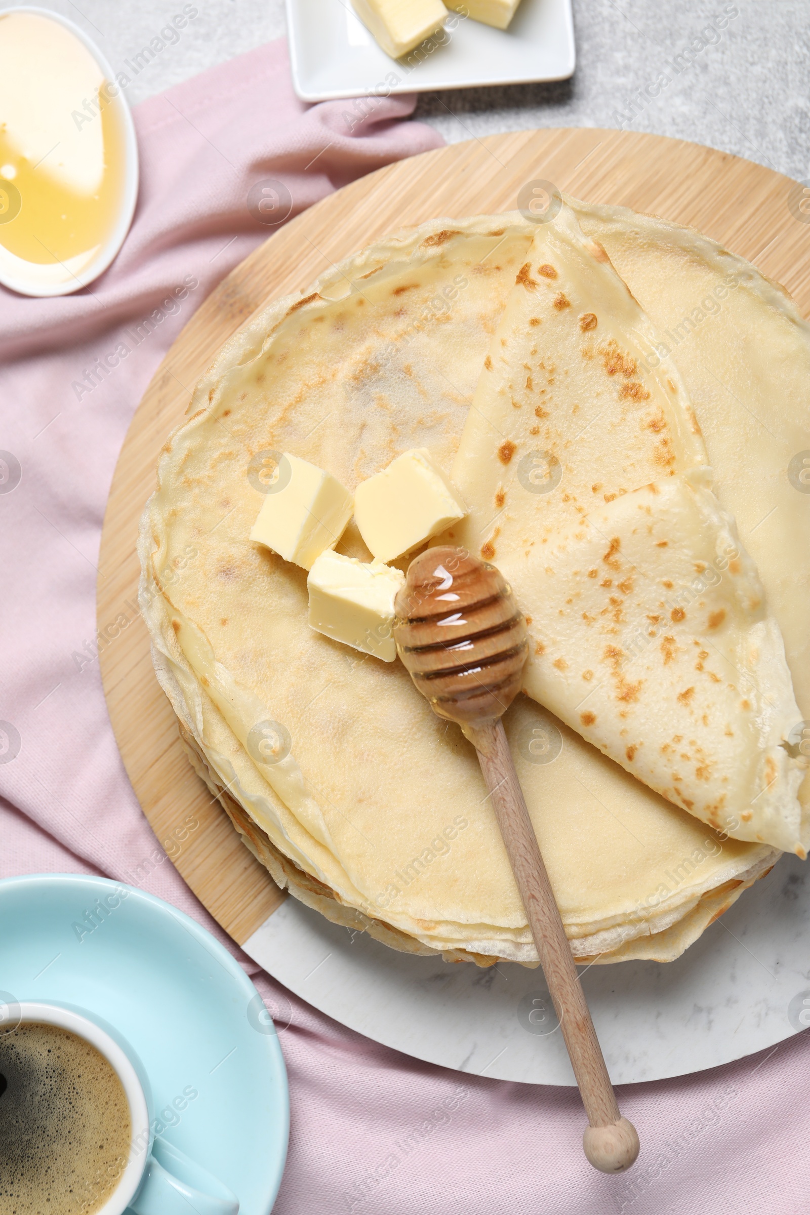 Photo of Tasty crepes with butter and honey served on grey textured table, flat lay