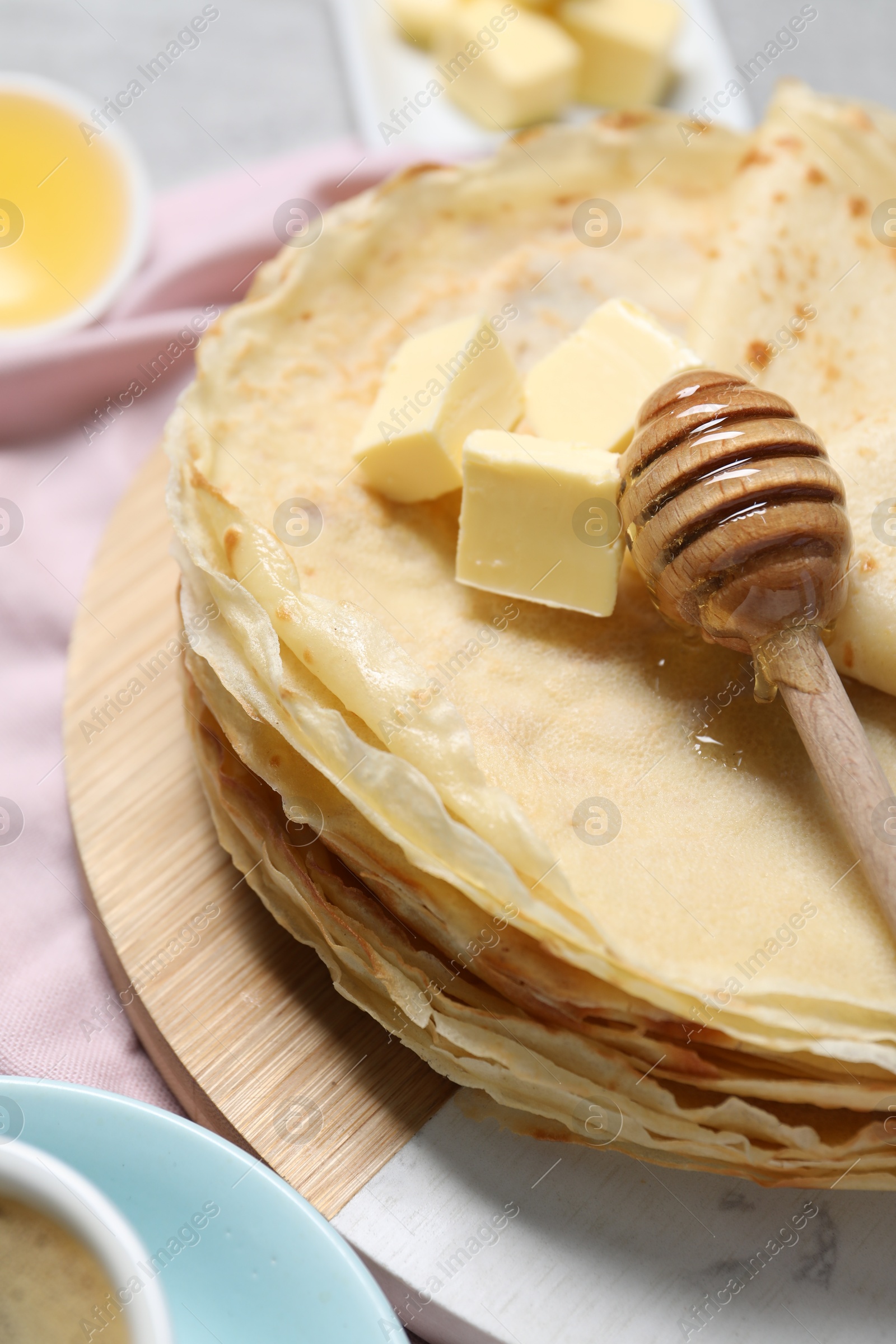 Photo of Tasty crepes with butter and honey on table, closeup