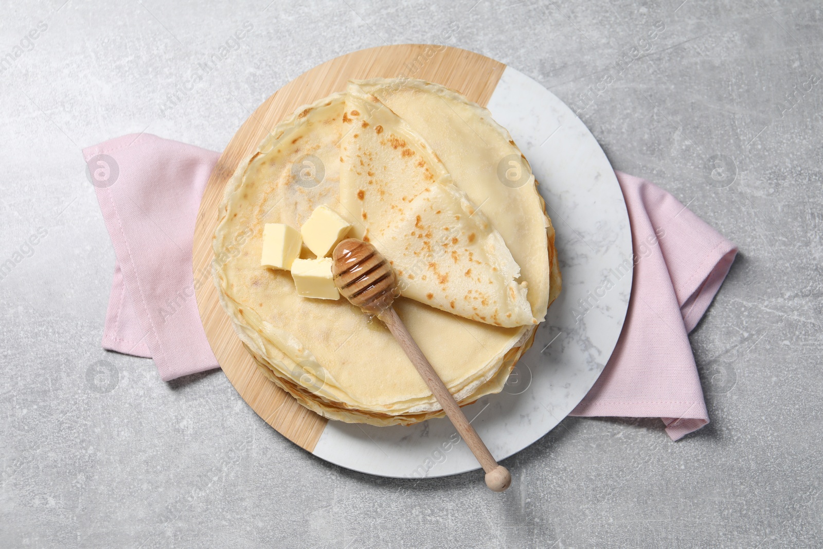 Photo of Tasty crepes with butter and honey on grey textured table, top view