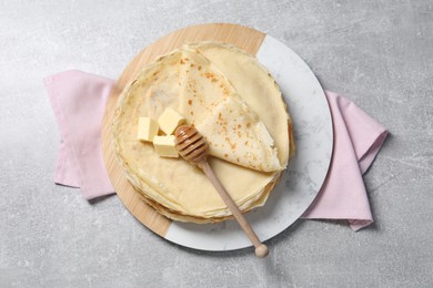 Photo of Tasty crepes with butter and honey on grey textured table, top view