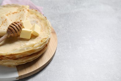 Photo of Tasty crepes with butter and honey on grey textured table, closeup. Space for text