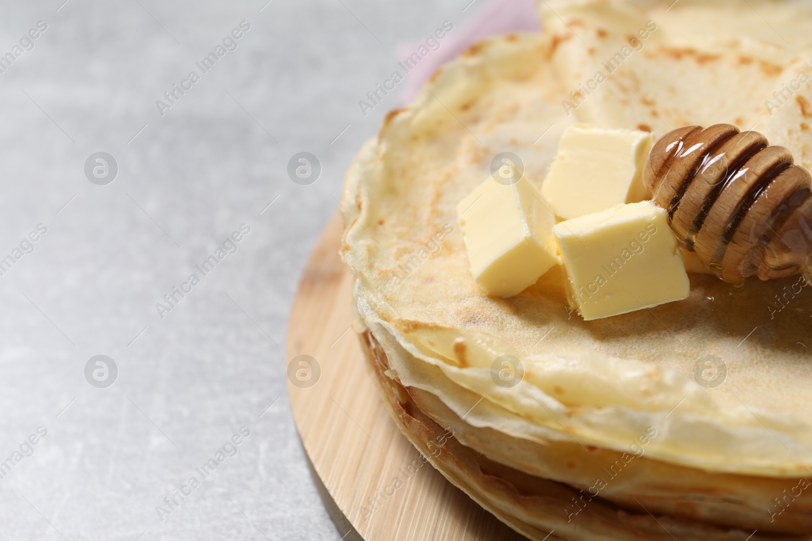 Photo of Tasty crepes with butter and honey on grey textured table, closeup. Space for text