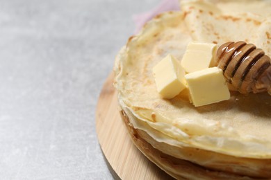 Photo of Tasty crepes with butter and honey on grey textured table, closeup. Space for text