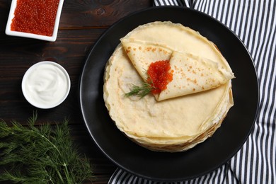 Photo of Tasty crepes with red caviar, dill and sauce on wooden table, flat lay