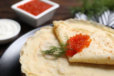 Photo of Tasty crepes with red caviar and dill on table, closeup