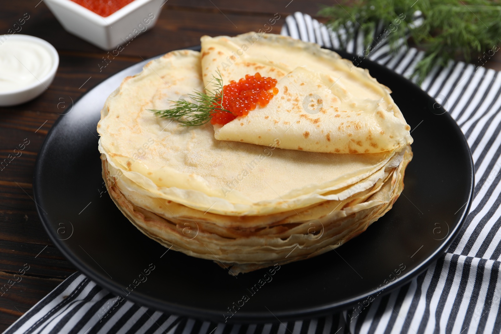 Photo of Tasty crepes with red caviar and dill on wooden table, closeup