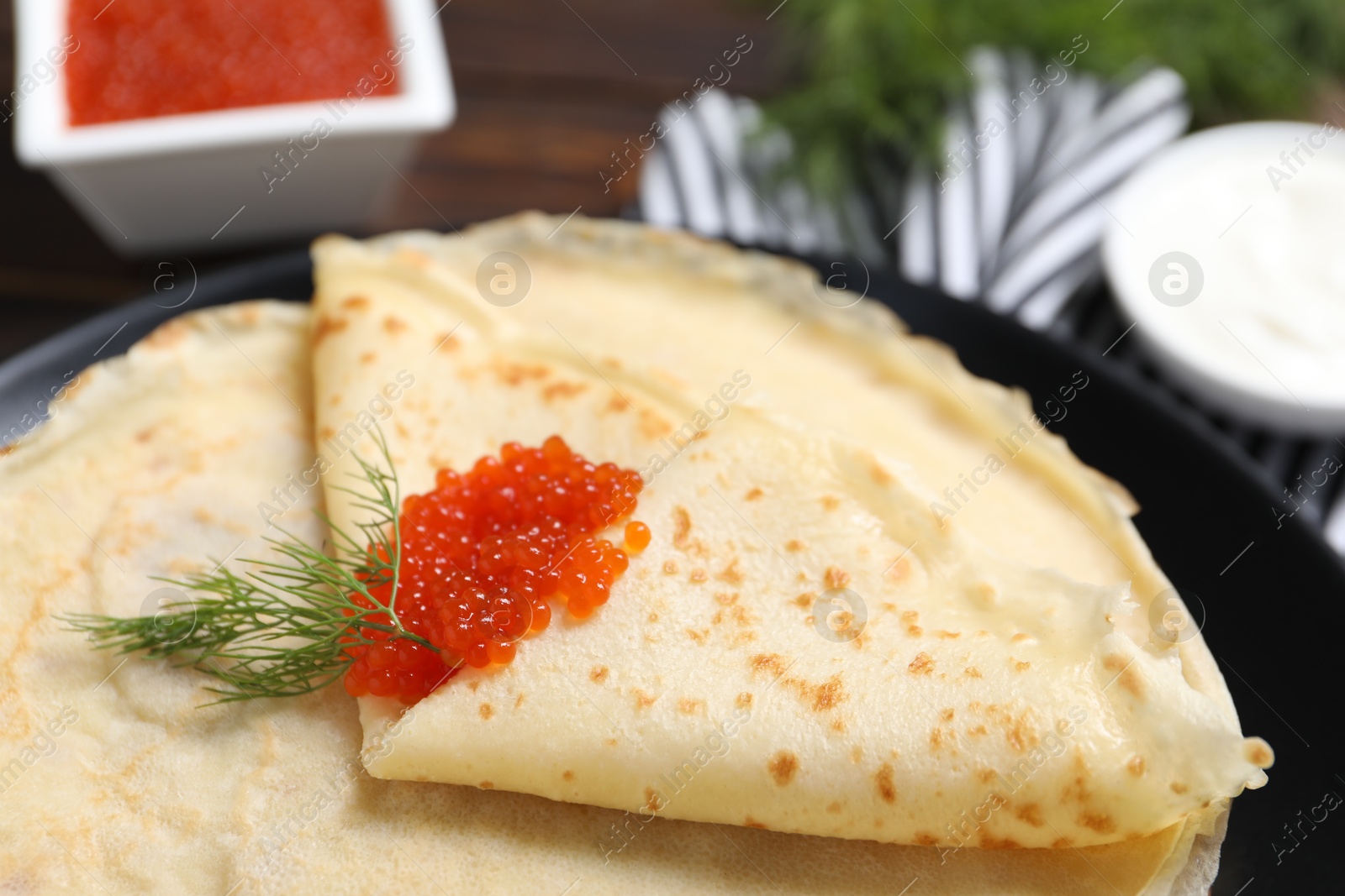 Photo of Tasty crepes with red caviar and dill on table, closeup