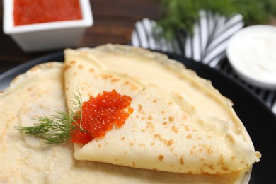 Photo of Tasty crepes with red caviar and dill on table, closeup