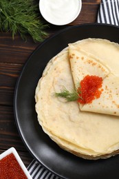 Photo of Tasty crepes with red caviar, dill and sauce on wooden table, flat lay