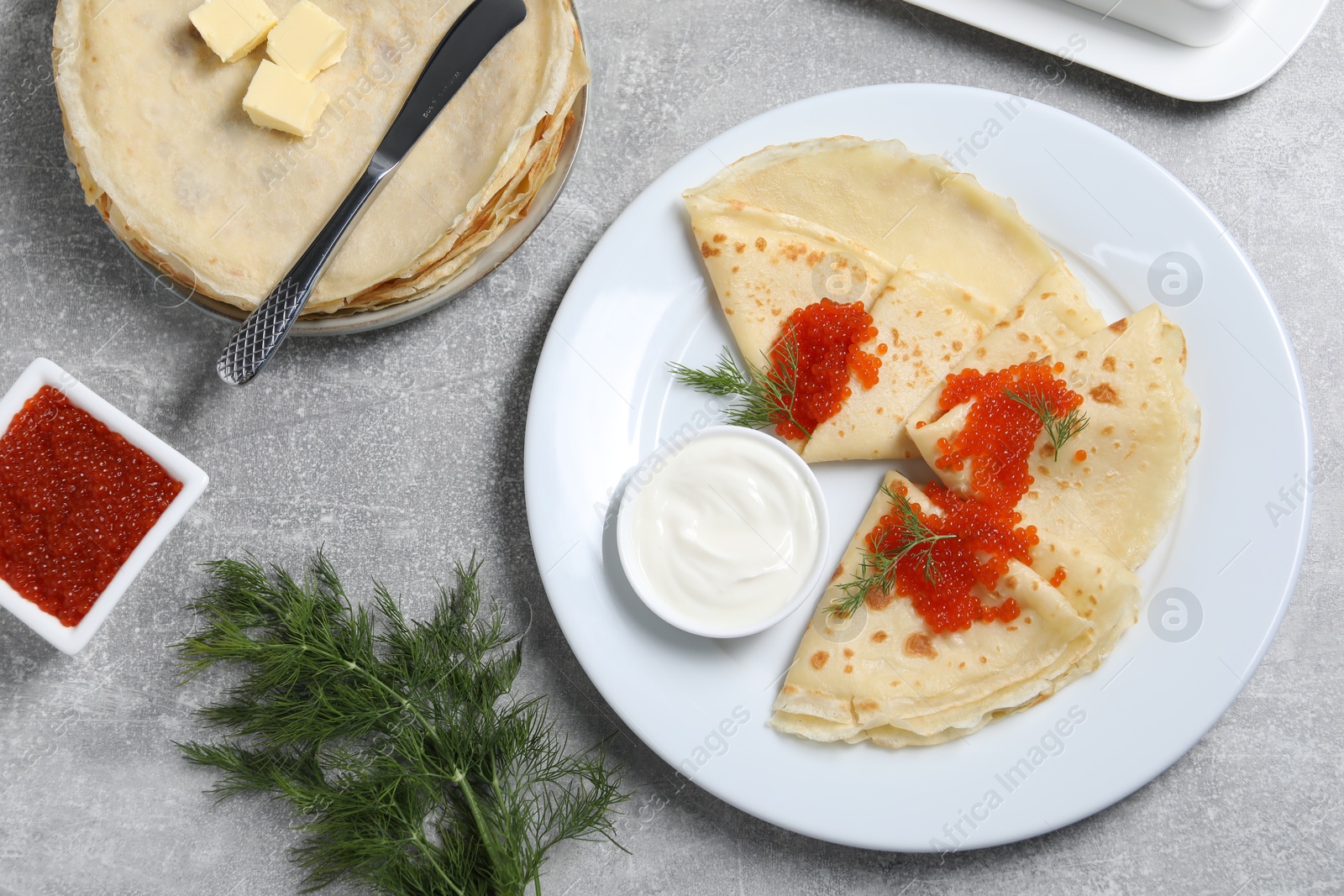 Photo of Tasty crepes with red caviar, dill and sauce served on grey textured table, flat lay