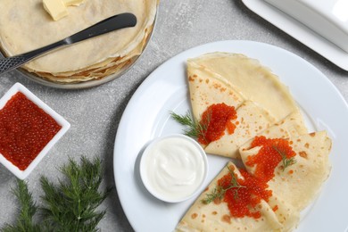 Photo of Tasty crepes with red caviar, dill and sauce served on grey textured table, flat lay