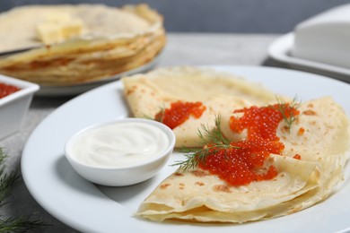 Photo of Tasty crepes with red caviar, dill and sauce on grey table, closeup