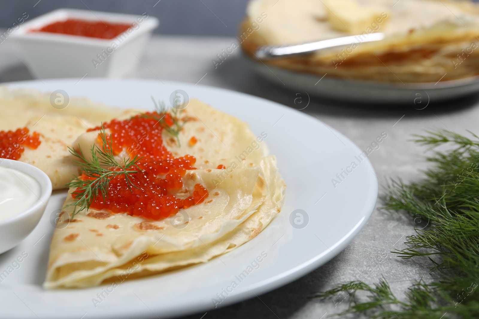 Photo of Tasty crepes with red caviar, dill and sauce on grey table, closeup