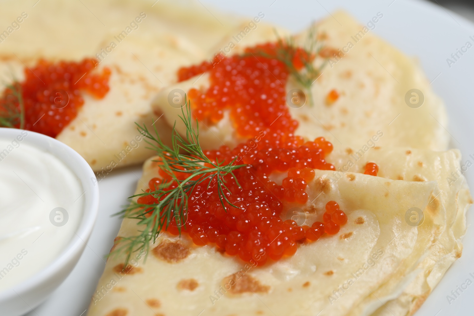 Photo of Tasty crepes with red caviar, dill and sauce on plate, closeup