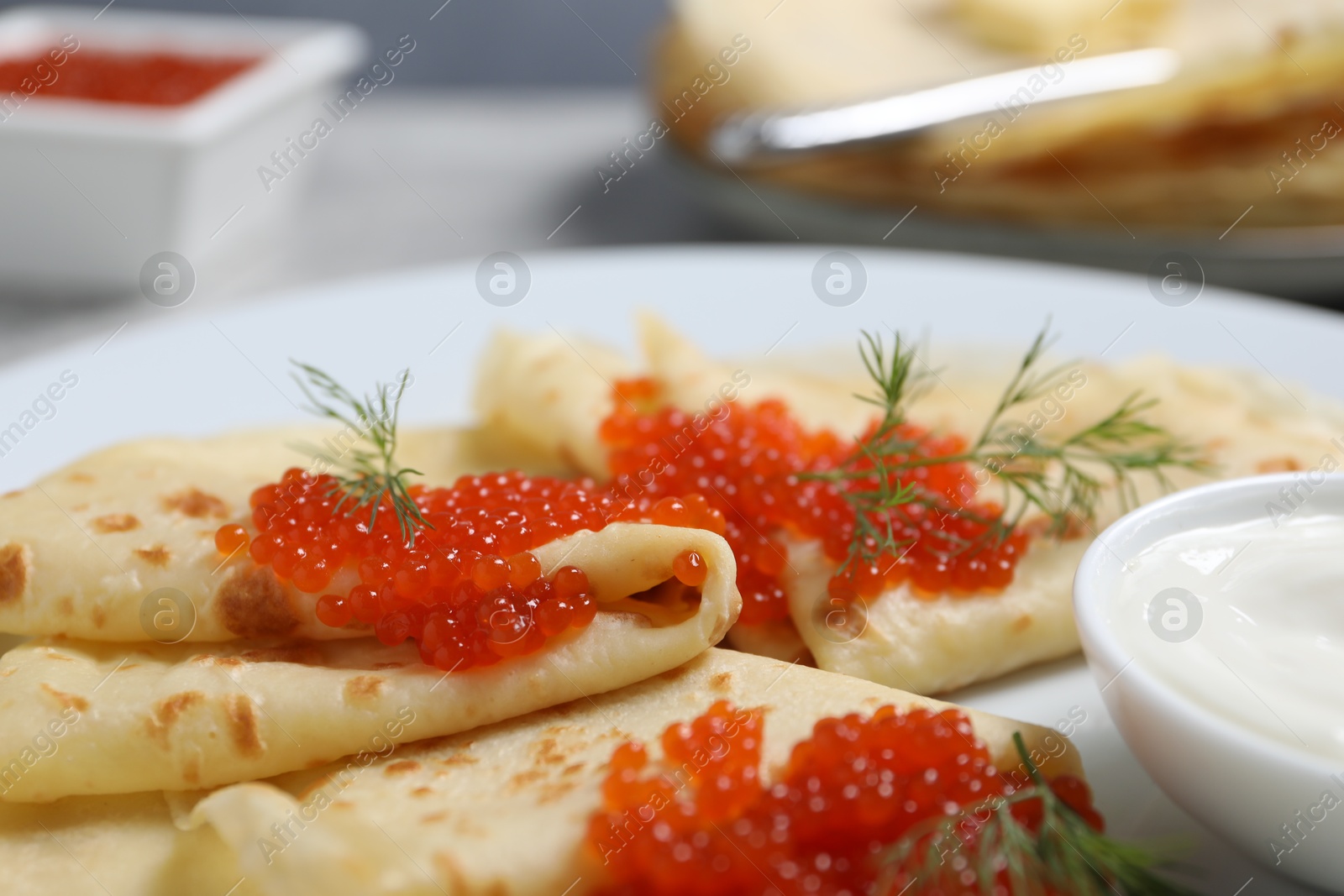 Photo of Tasty crepes with red caviar, dill and sauce on grey table, closeup