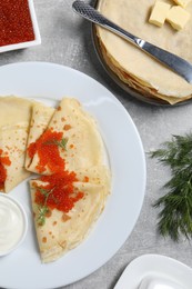 Photo of Tasty crepes with red caviar, dill and sauce served on grey textured table, flat lay