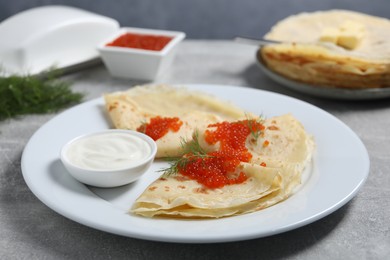 Photo of Tasty crepes with red caviar, dill and sauce on grey textured table, closeup