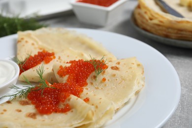 Photo of Tasty crepes with red caviar, dill and sauce on grey table, closeup