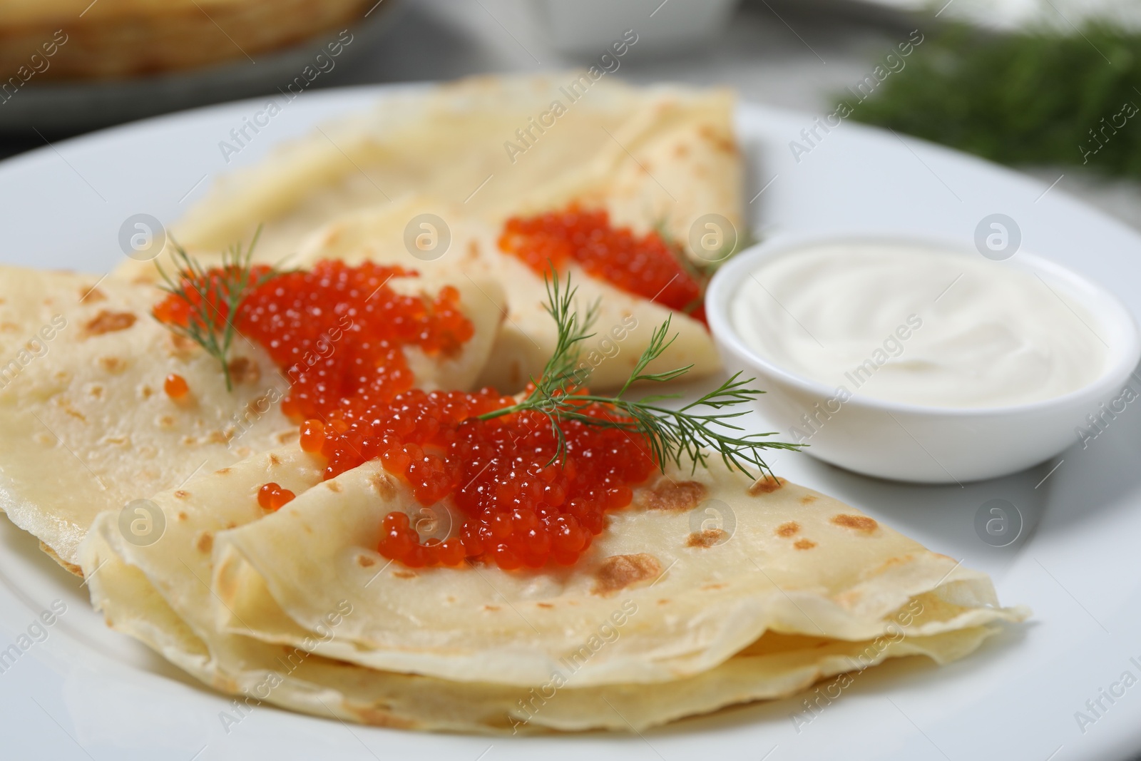 Photo of Tasty crepes with red caviar, dill and sauce on plate, closeup